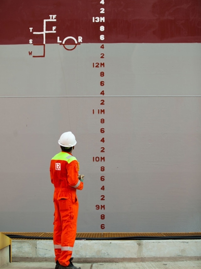 Worker on outside of ship looking at markings.