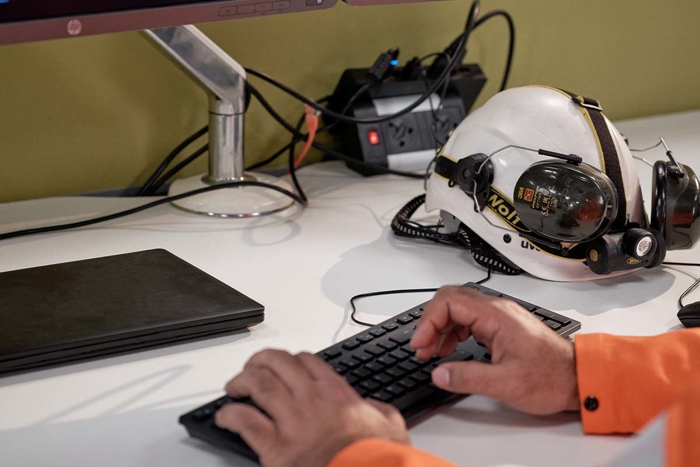 Hands of someone in a high visibility boiler suit, typing at a keyboard.  The screen has LR logos on it.